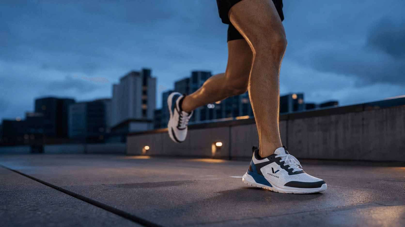 Runner wearing a white, black and blue KOMVANO SPORT concept shoe on an urban route at blue hour.